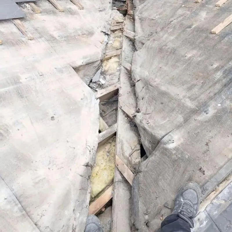 Exposed damaged roof valley with torn underlay and timber visible beneath the removed slates