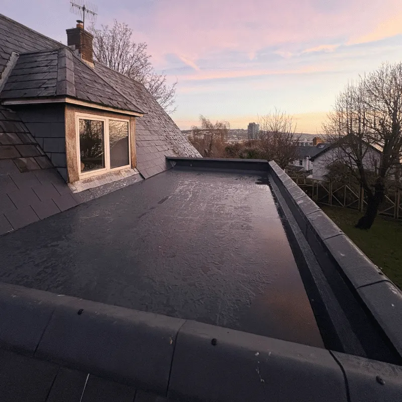 Completed flat-roof covering with raised edge details beside a slate-clad dormer