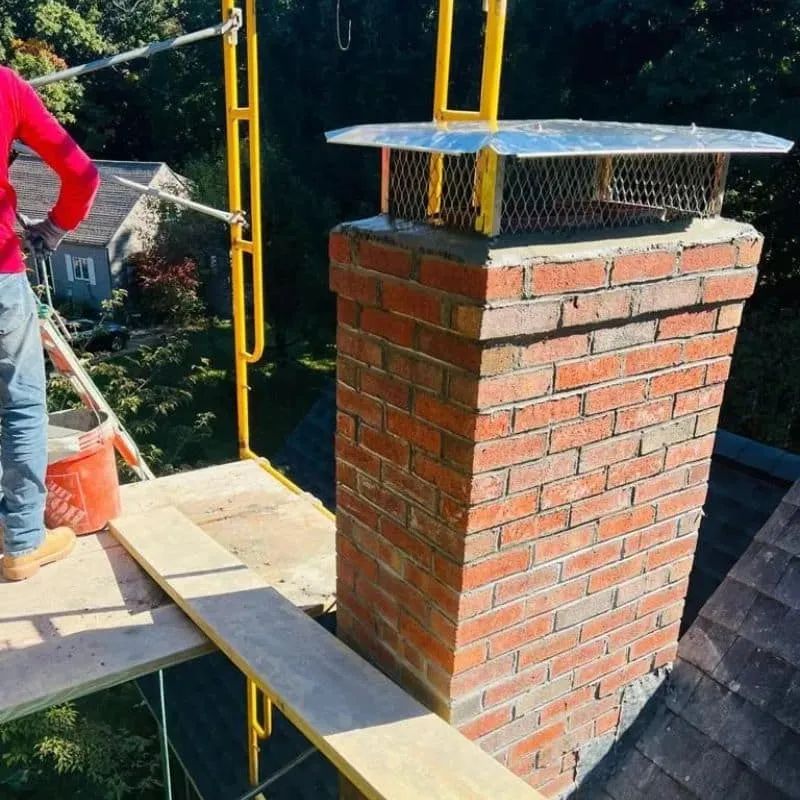 Brick chimney stack with visible mortar joints and metal top covers, surrounded by scaffolding
