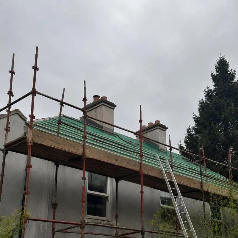 Two rendered chimney stacks above a roof with exposed battens and scaffolding