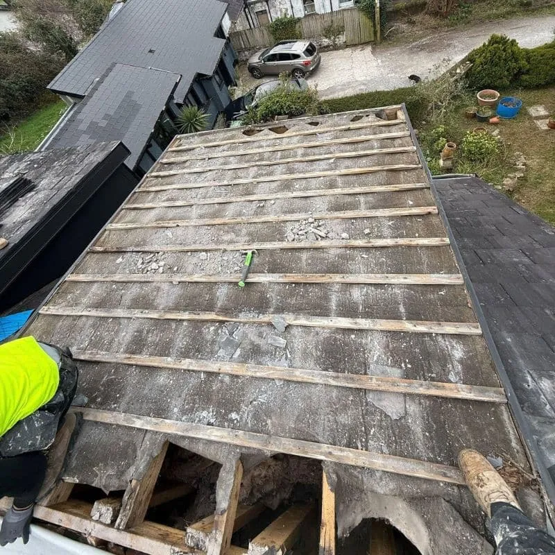 Dormer roof with natural slates removed, exposing battens and torn roofing membrane